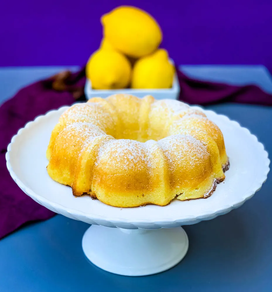 air fryer lemon cake on a white cake stand with fresh lemons