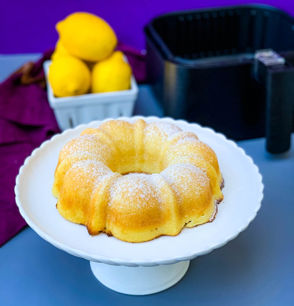 air fryer lemon cake on a white cake stand with fresh lemons