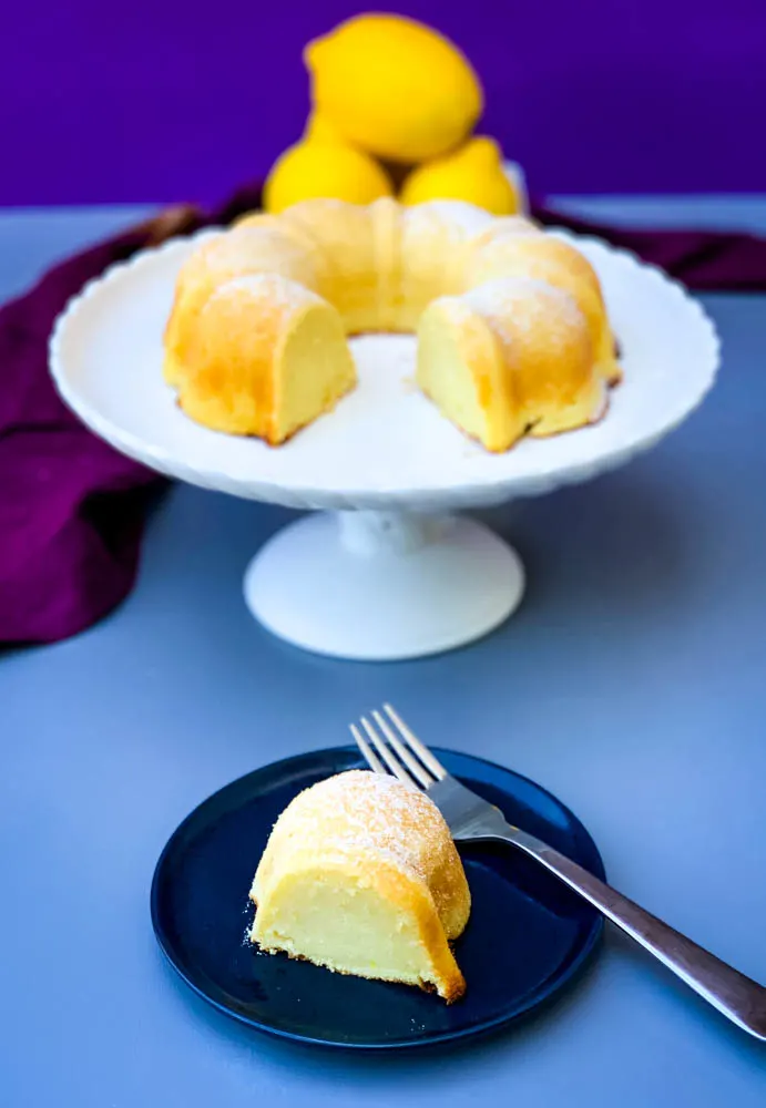 air fryer lemon cake on a white cake stand with fresh lemons