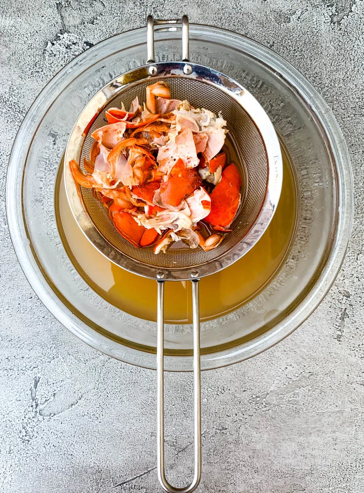 shelled lobster in a strainer with a bowl of lobster stock
