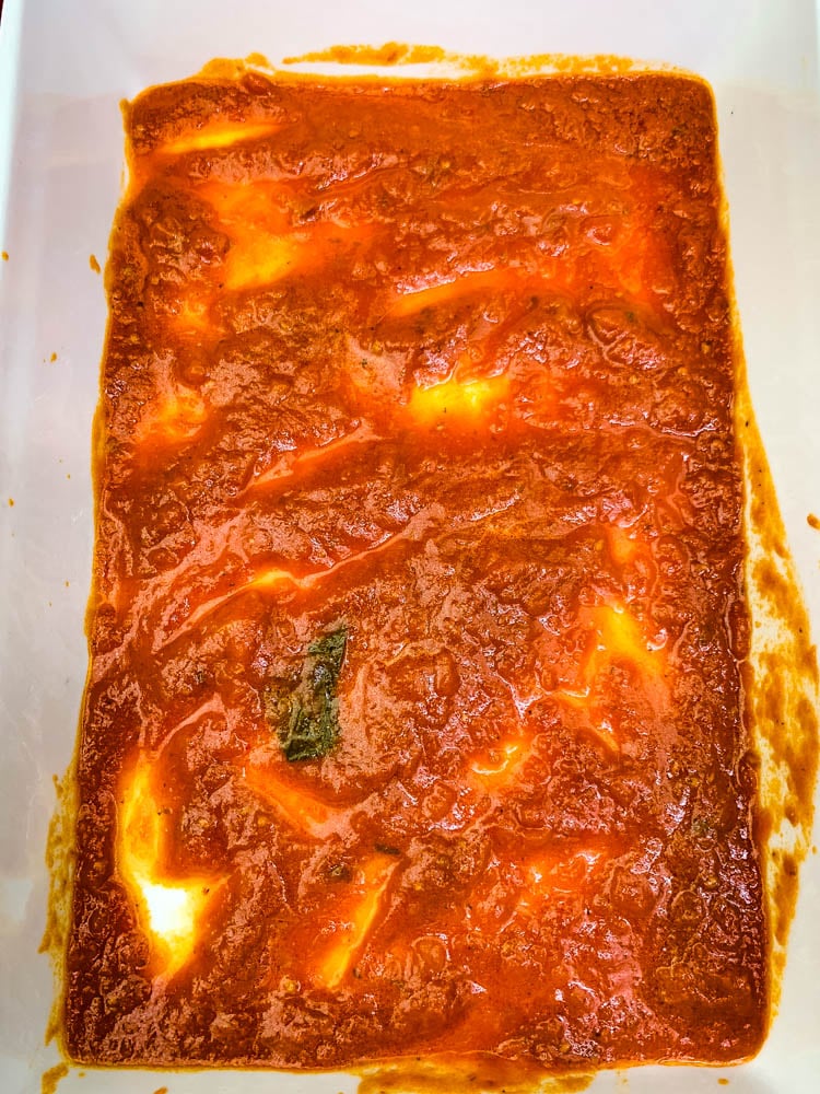 marinara in the bottom of a white baking dish