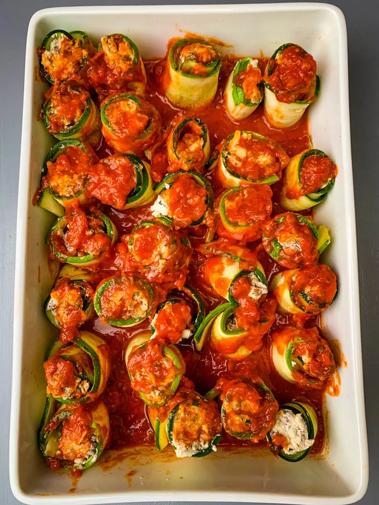 zucchini lasagna rolls with marinara in a white baking dish