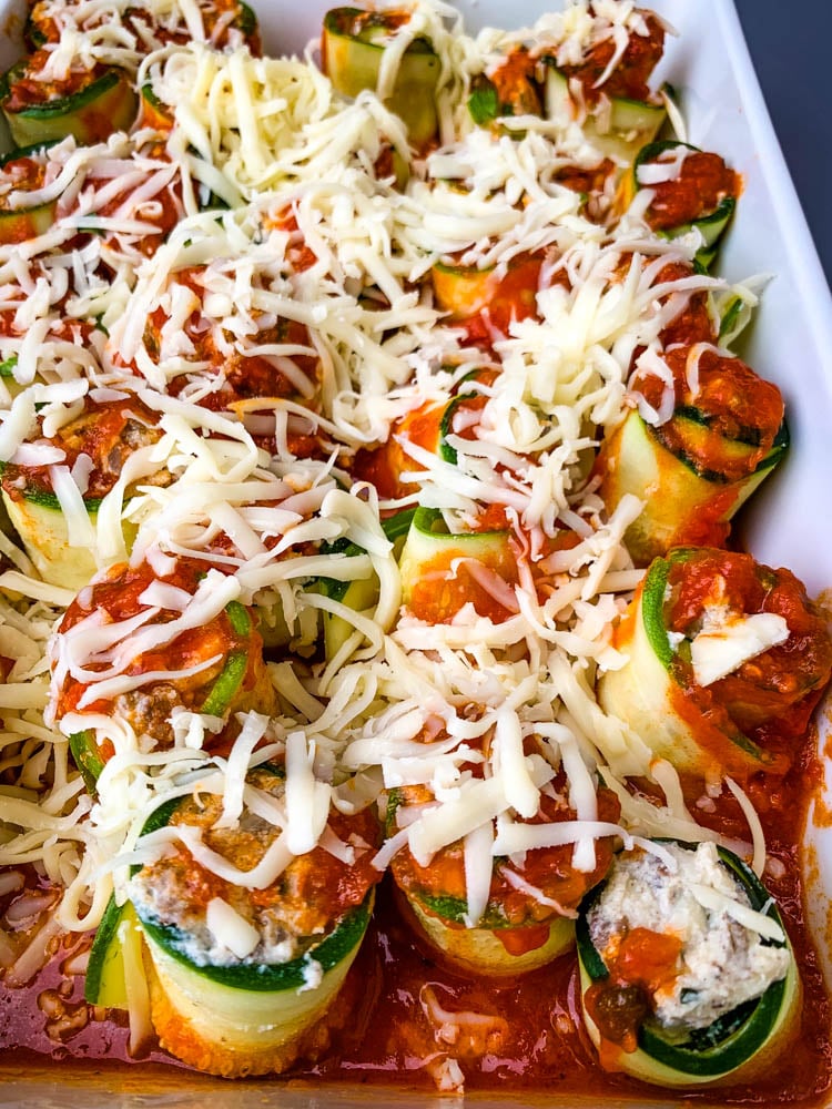 zucchini lasagna roll ups in a white baking pan with shredded cheese