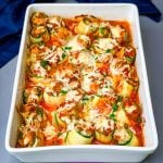 zucchini lasagna roll ups in a white baking pan with shredded cheese