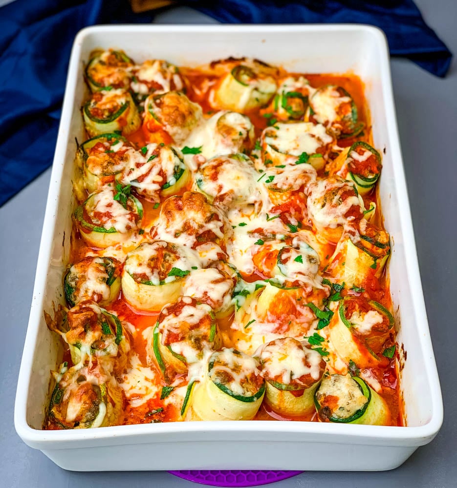 zucchini lasagna roll ups in a white baking pan with shredded cheese