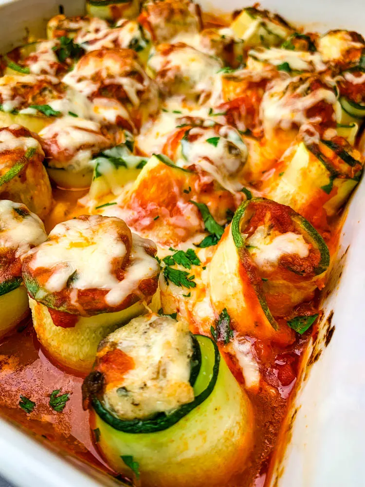 zucchini lasagna roll ups in a white baking pan with shredded cheese