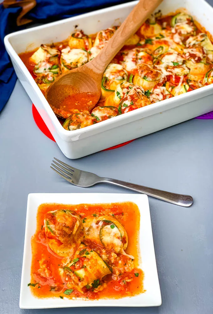 zucchini lasagna roll ups in a white baking pan with shredded cheese and white plate with zucchini rolls