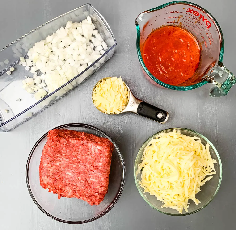 chopped onions, raw ground beef, marinara, and shredded cheese in glass bowls for zucchini lasagna roll ups