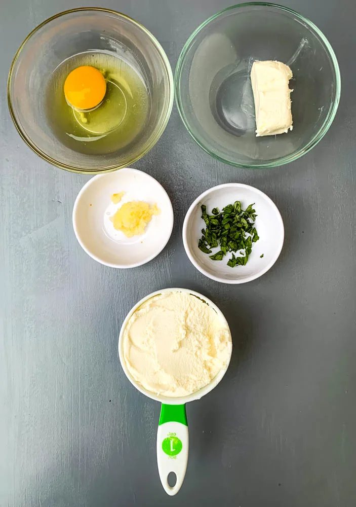 egg, cream cheese, ricotta, garlic, and basil in separate bowls for zucchini lasagna roll ups