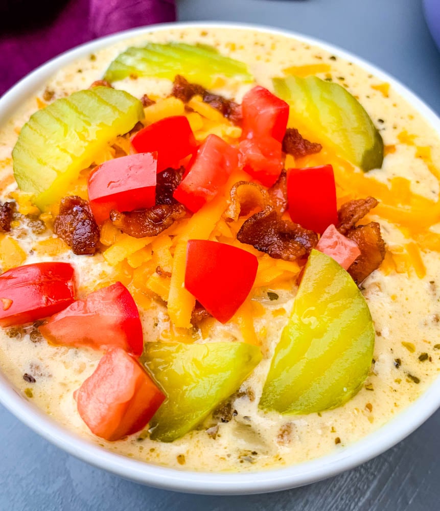 keto low carb cheeseburger soup in a white bowl with pickles, tomatoes, and bacon