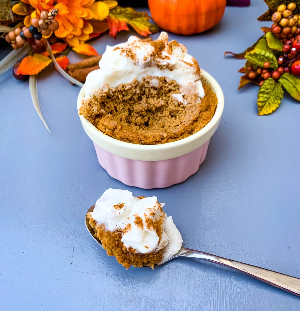 a spoon serving of keto low carb pumpkin mug cake in a pink ramekin with whipped cream