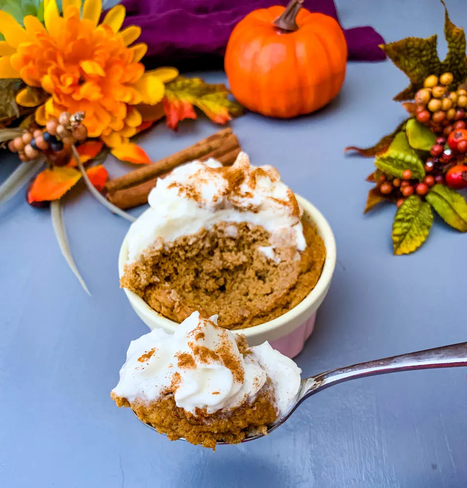 a spoon serving of keto low carb pumpkin mug cake in a pink ramekin with whipped cream