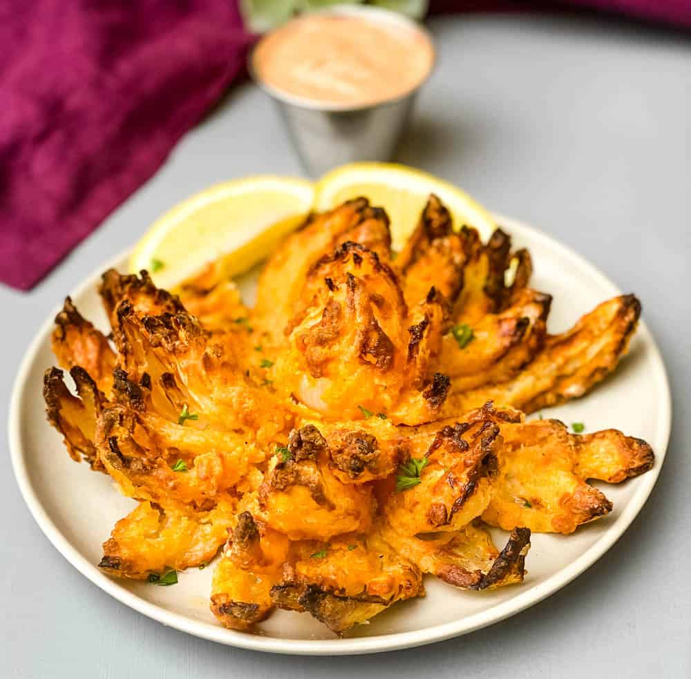 air fryer blooming onion on a plate with sliced lemons