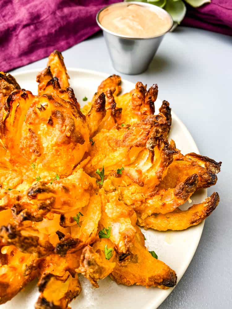 air fryer blooming onion on a plate with sliced lemons