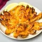 air fryer blooming onion on a plate with sliced lemons