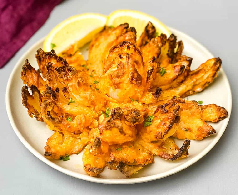 air fryer blooming onion on a plate with sliced lemons