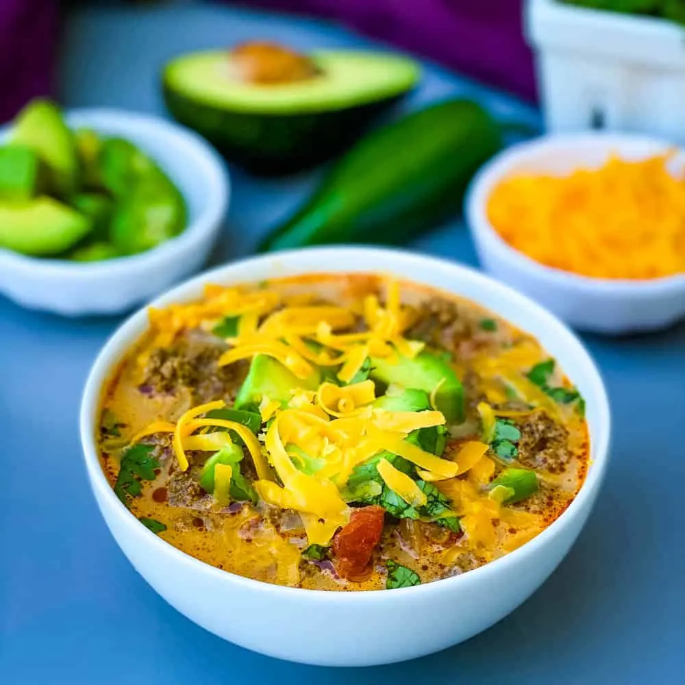 keto low carb taco soup with shredded cheese, avocado, and jalapenos in a white bowl