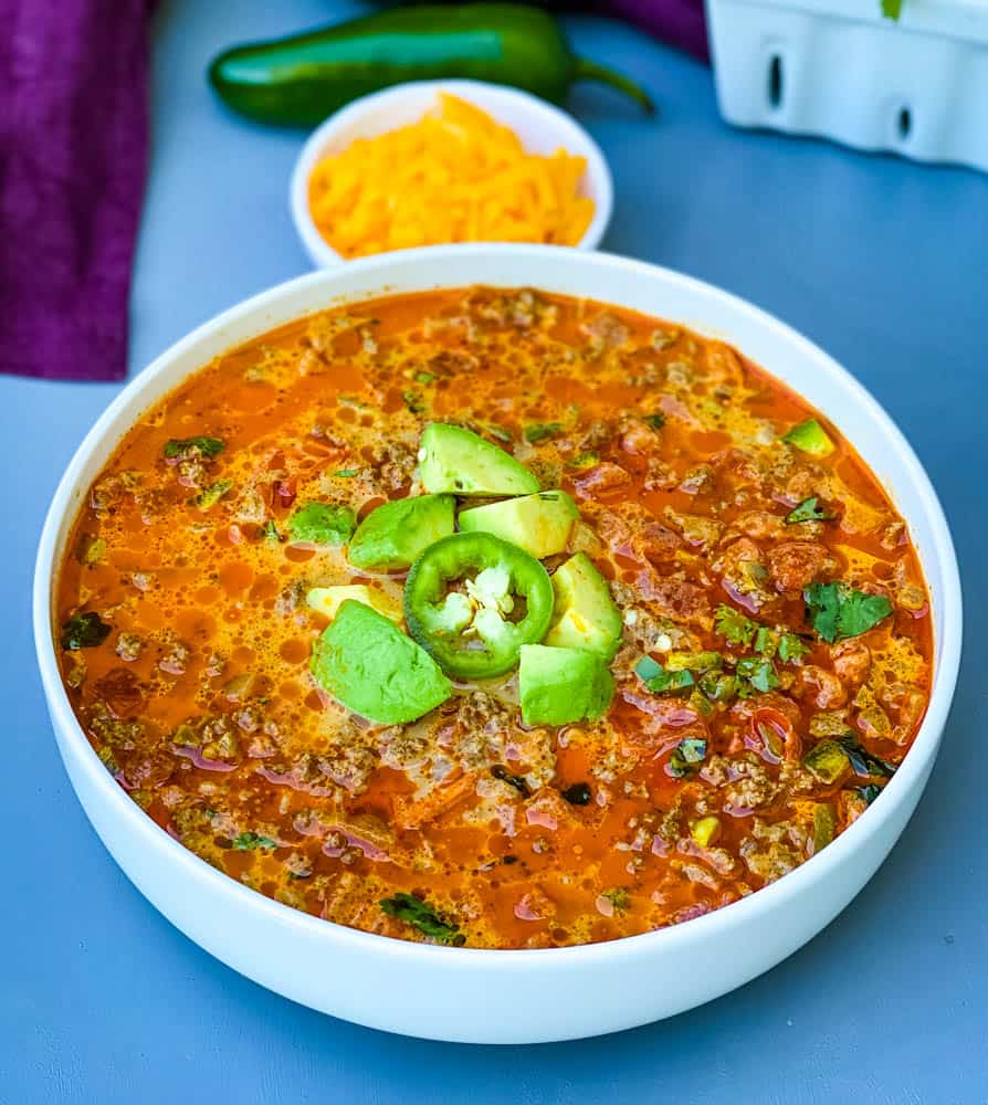 keto low carb taco soup with shredded cheese, avocado, and jalapenos in a white bowl