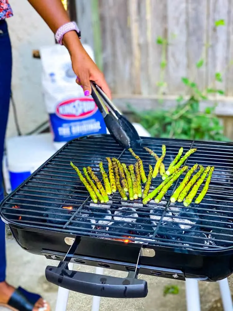 person grilling asparagus on a charcoal grill