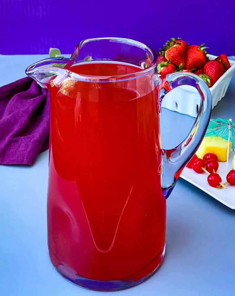 easy rum punch in a glass pitcher with fresh pineapples and cherries