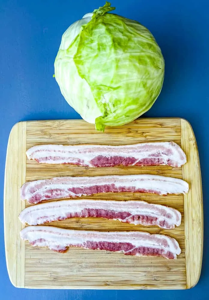 raw green cabbage head and raw bacon slices on a cutting board for southern fried cabbage