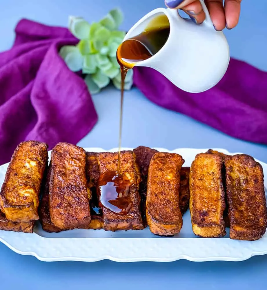air fryer french toast sticks on a white plate with syrup drizzled throughout