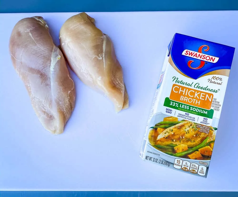 raw chicken breasts on a cutting board with a box of chicken broth