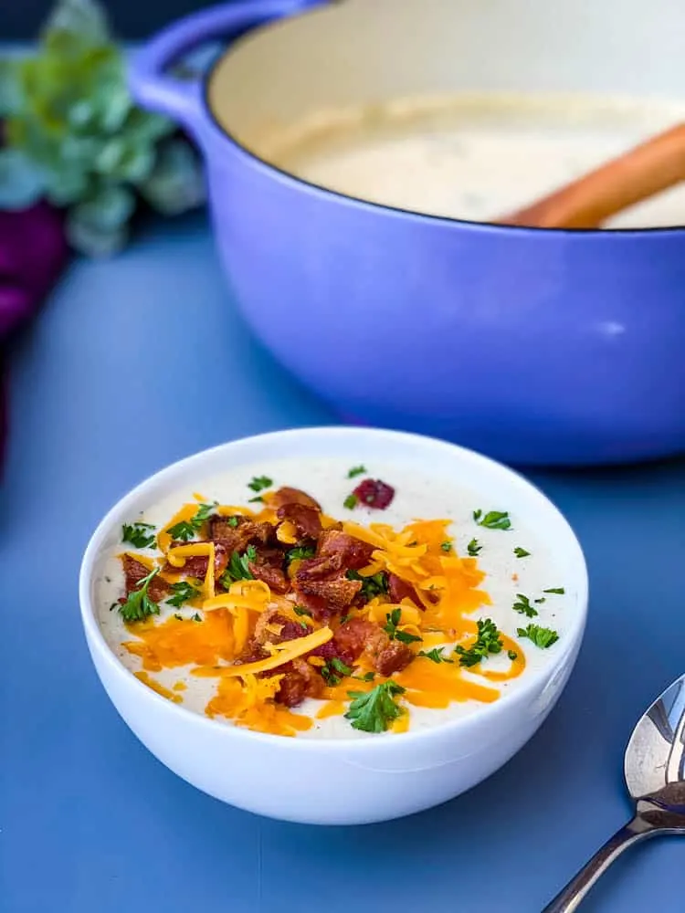keto low carb cauliflower soup in a white bowl with shredded cheese and bacon