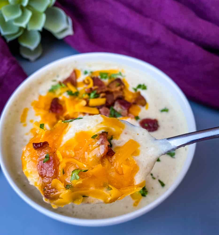 spoonful of keto low carb cauliflower soup in a white bowl with shredded cheese and bacon