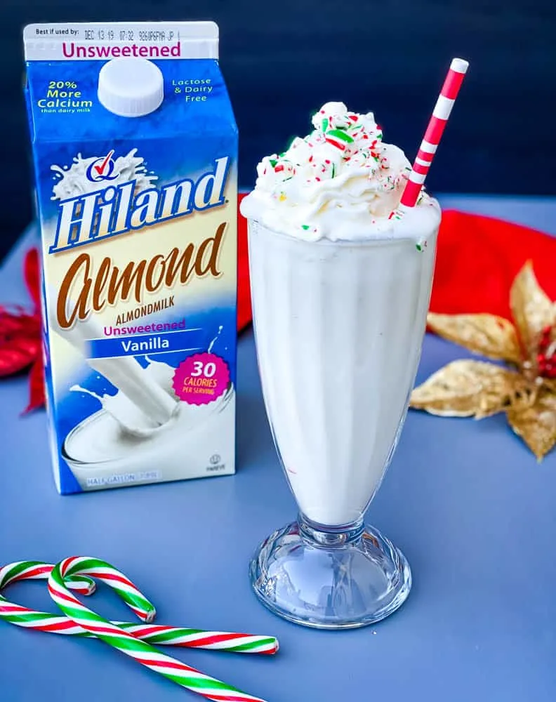 peppermint milkshake with candy canes and whipped cream in a glass with a straw alongside a carton of Almond milk