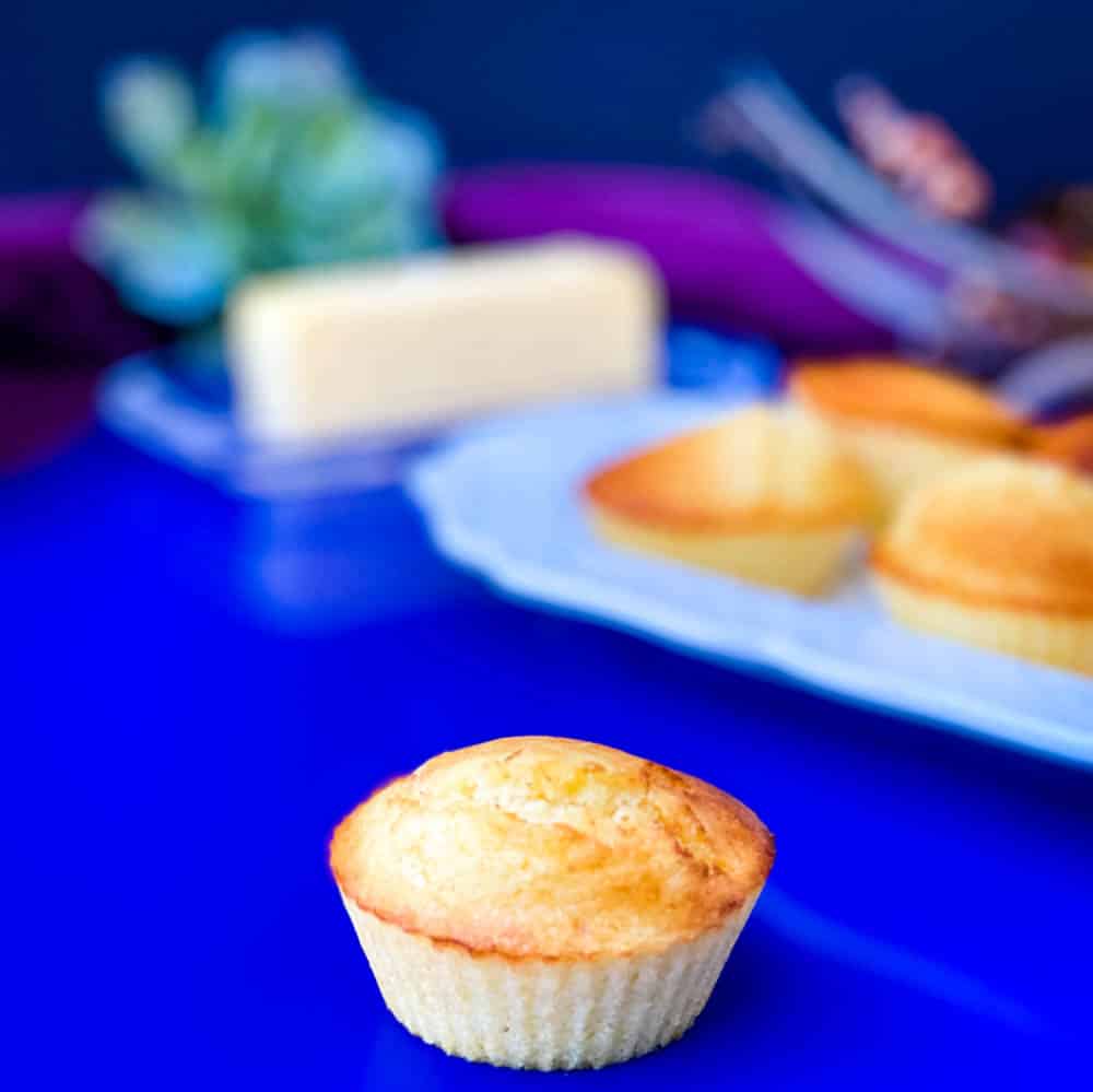 air fryer cornbread muffin on a blue plate with several air fryer cornbread muffins on a white plate