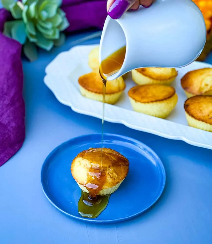 honey being drizzled on air fryer cornbread muffin on a blue plate with several air fryer cornbread muffins on a white plate