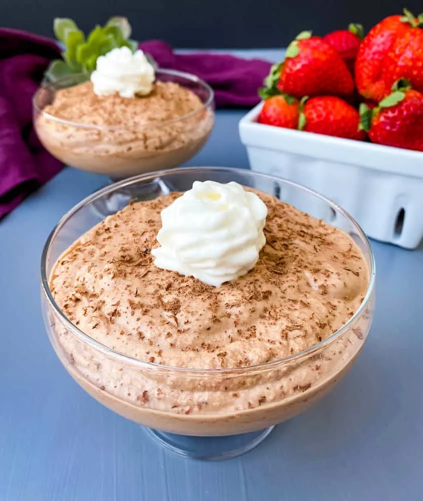 keto low carb chocolate mousse in a glass bowl with a white bowl of fresh strawberries