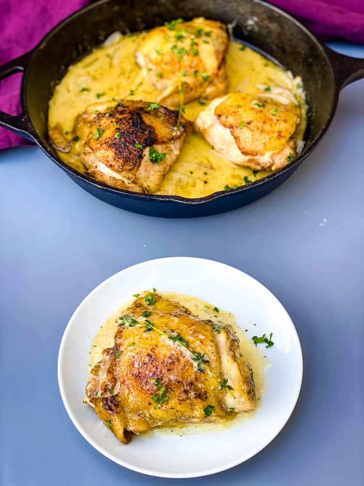 smothered pork chop thighs in a cast iron skillet with gravy with one chicken thigh serving on a white plate