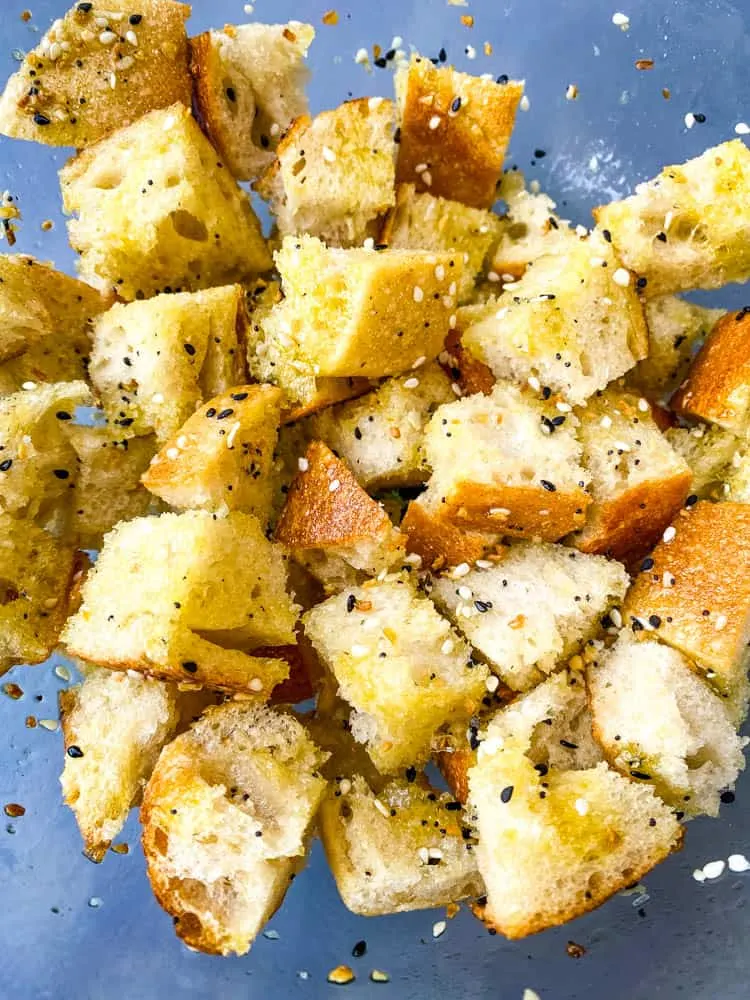 sliced sourdough bread in a glass bowl with olive oil and seasoning for air fryer croutons