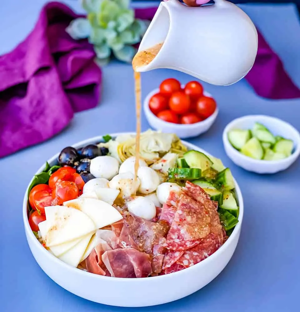 Italian dressing drizzled over antipasto salad in a white bowl