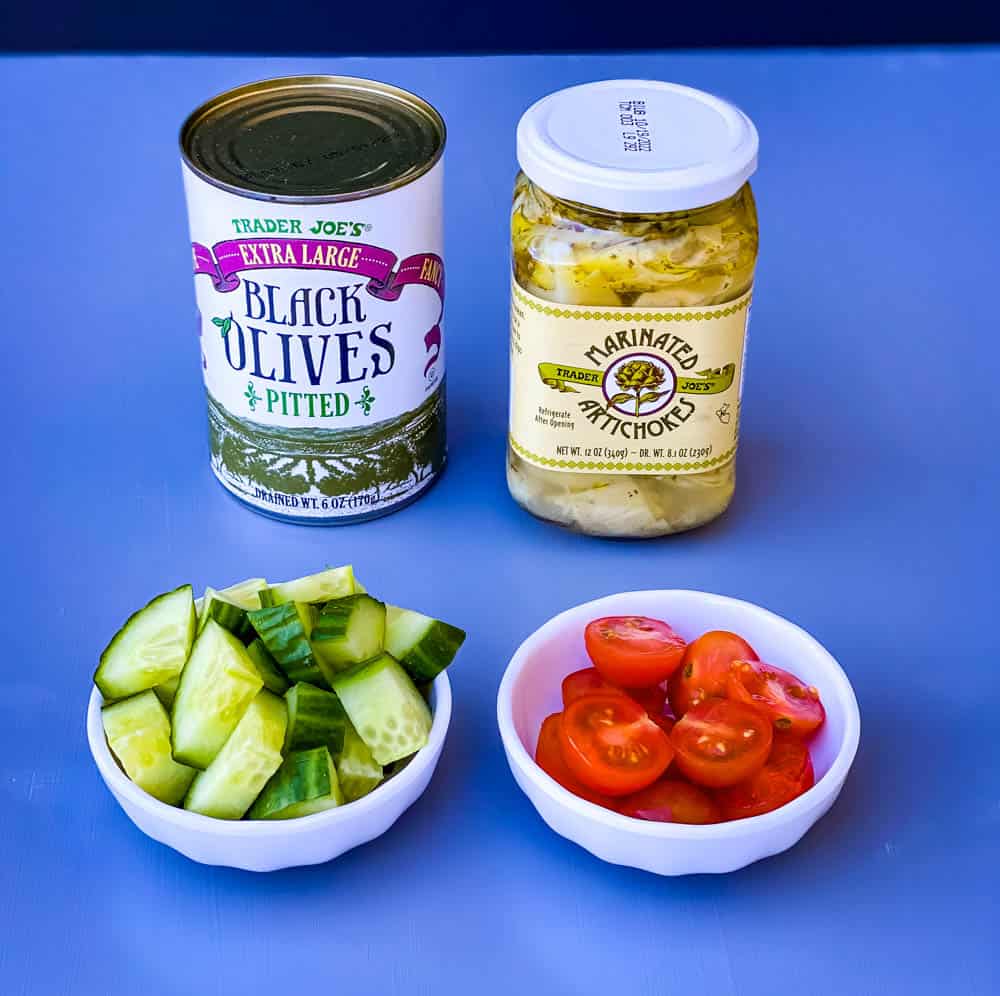 black olives, artichokes, cucumbers, and sliced cherry tomatoes in separate white bowls for antipasto salad recipe