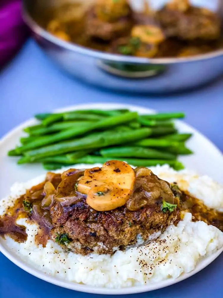 keto low carb salisbury steaks on mashed cauliflower with green beans on a white plate