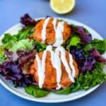 fresh salmon patties on a plate with mixed greens and creamy garlic sauce