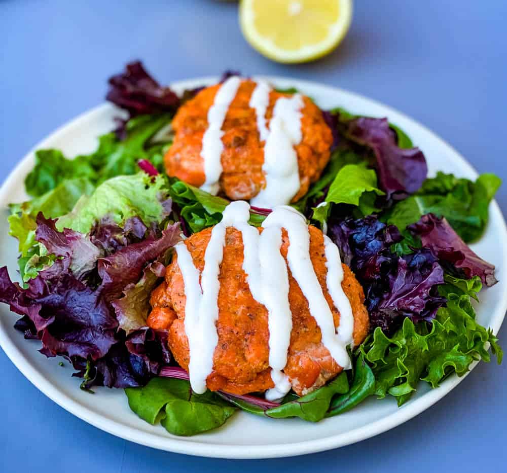 fresh salmon patties on a plate with mixed greens and creamy garlic sauce