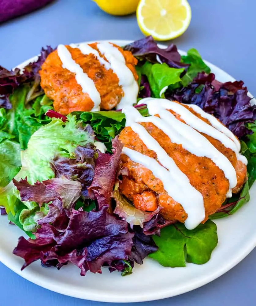 keto low carb salmon patties on a plate with mixed greens and creamy garlic sauce