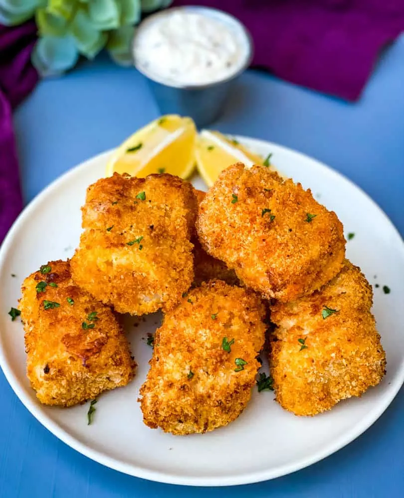 air fryer fish sticks on a white plate with tarter sauce and lemons