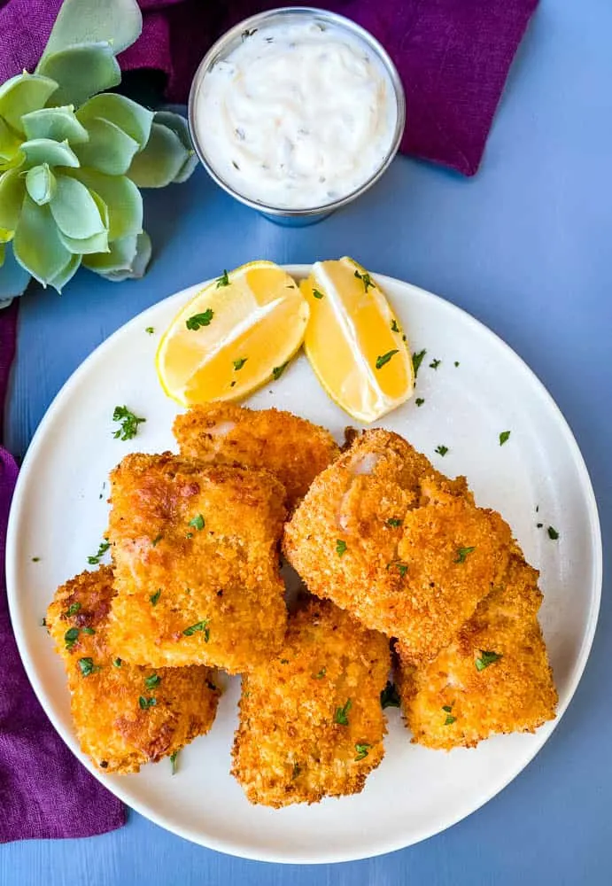 air fryer fish sticks on a white plate with tarter sauce and lemons