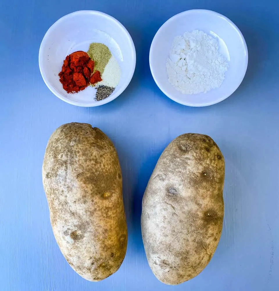 2 russet potatoes on a flat surface with flour and seasoning