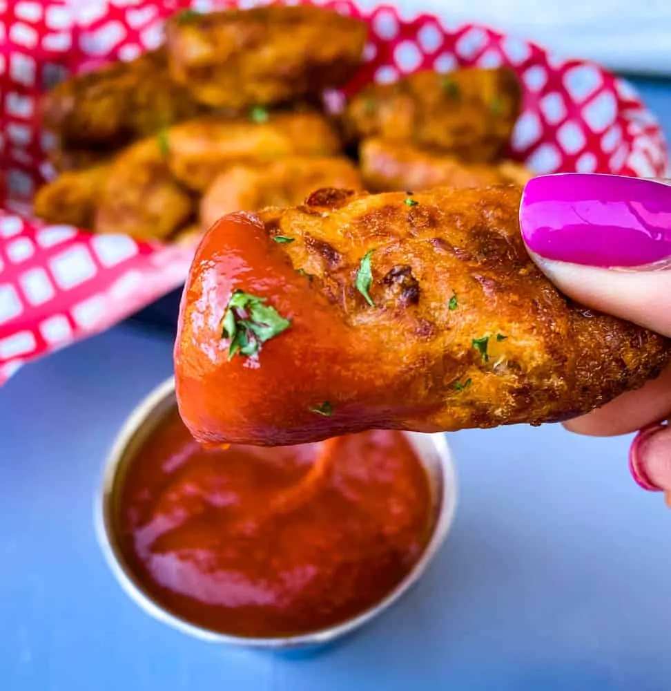 person holding air fryer tater tot with ketchup