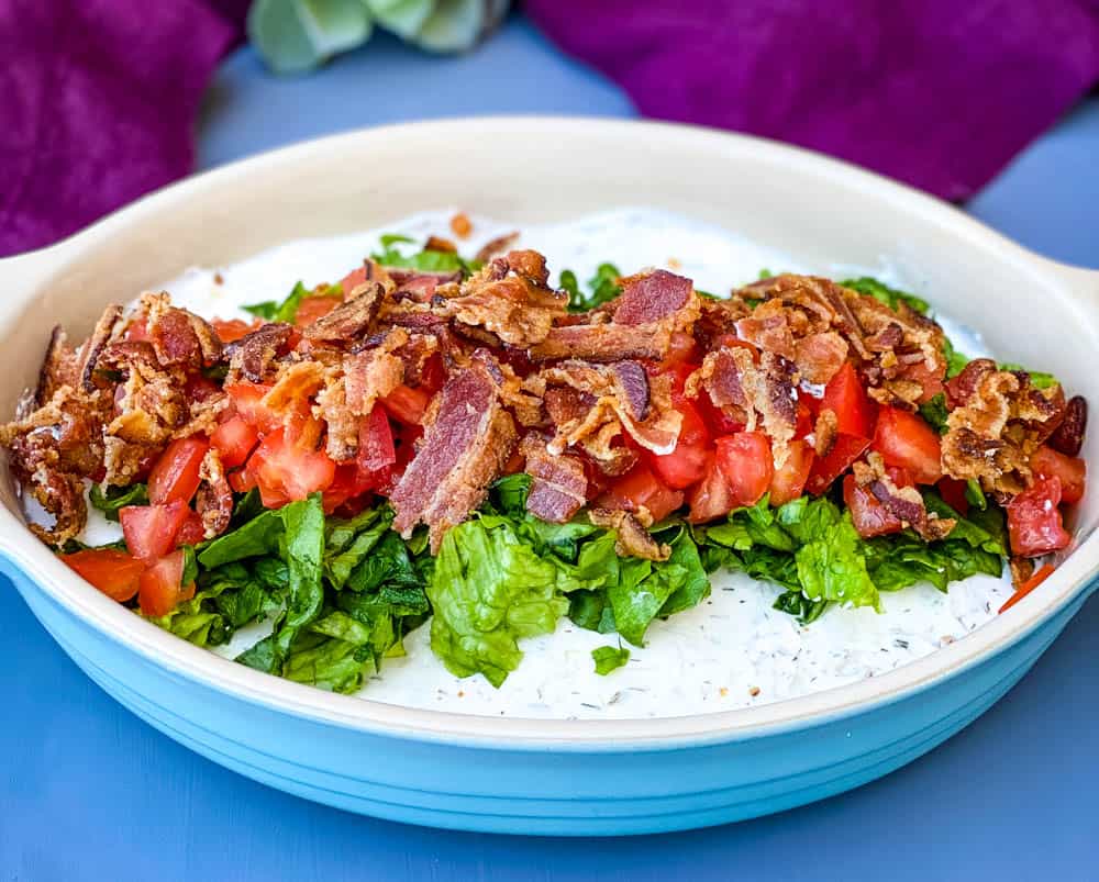 BLT dip with lettuce, bacon, and tomatoes in a blue serving dish