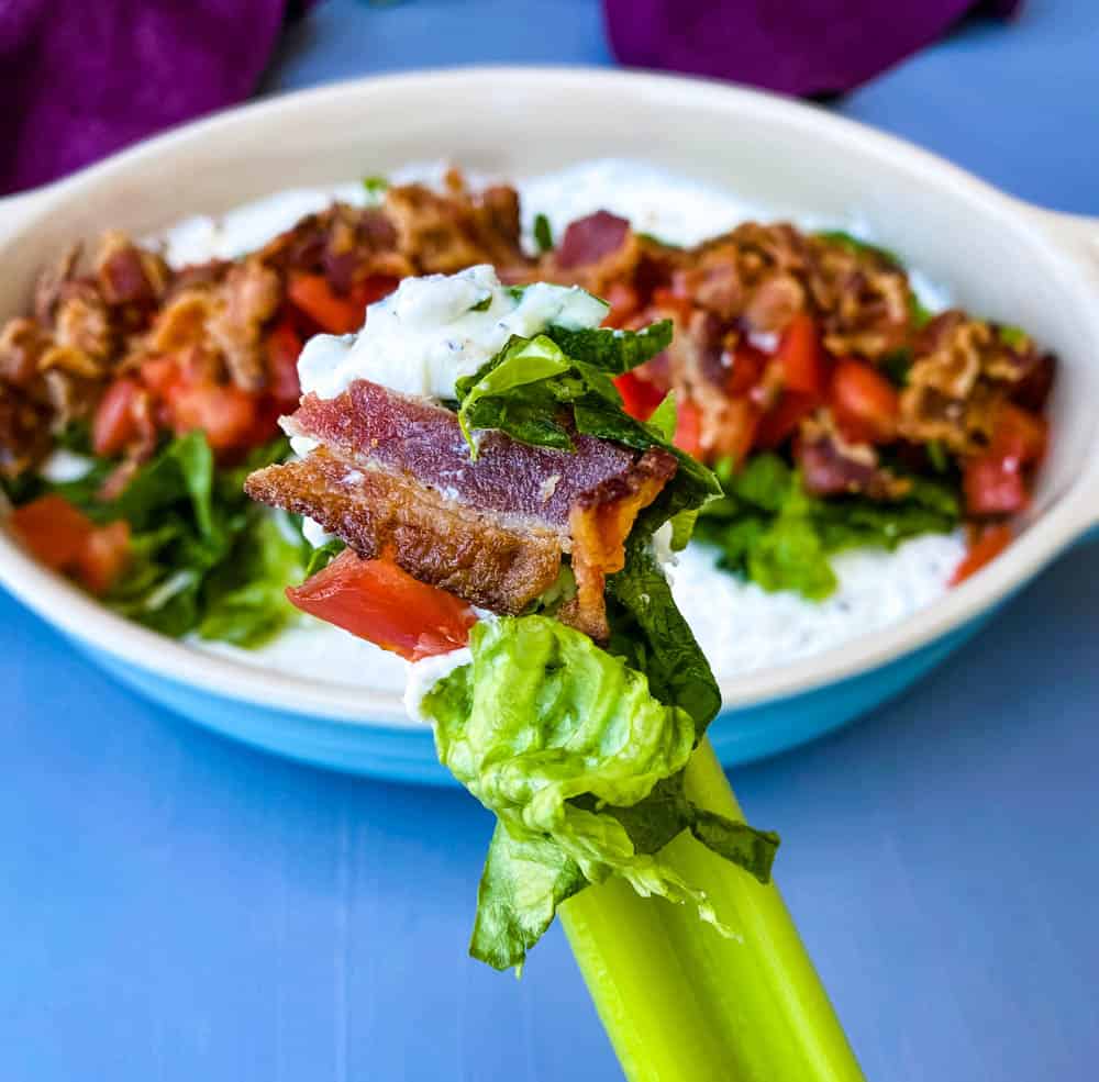 person holding BLT Dip with lettuce, bacon, and tomatoes on top of celery