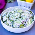 creamy cucumber salad with red onions in a white bowl