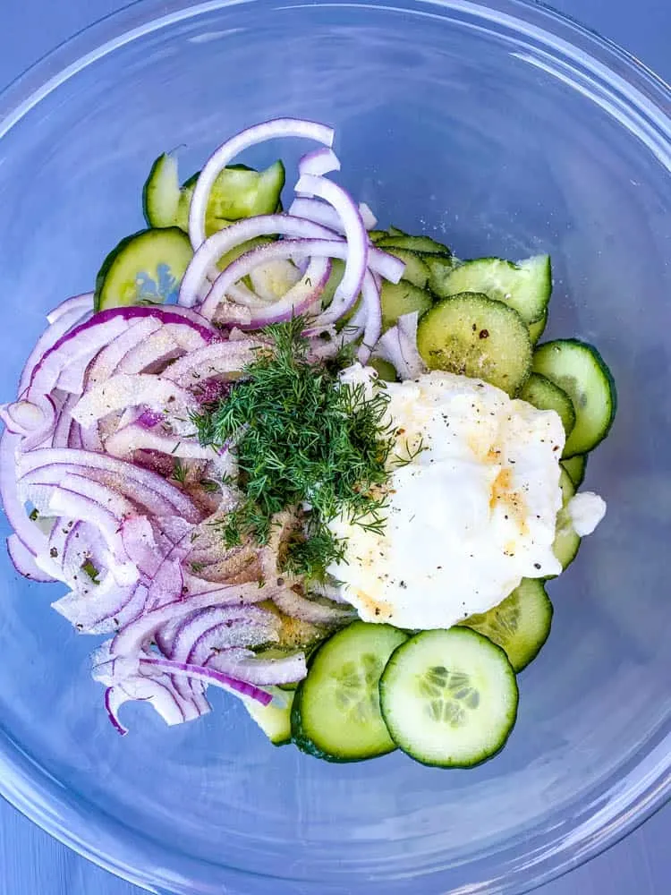 sliced cucumbers and onions in a glass bowl with Greek yogurt, lemon juice, seasoning, and fresh dill