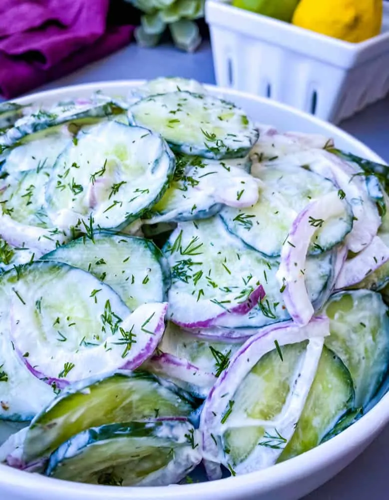 creamy cucumber salad with red onions in a white bowl